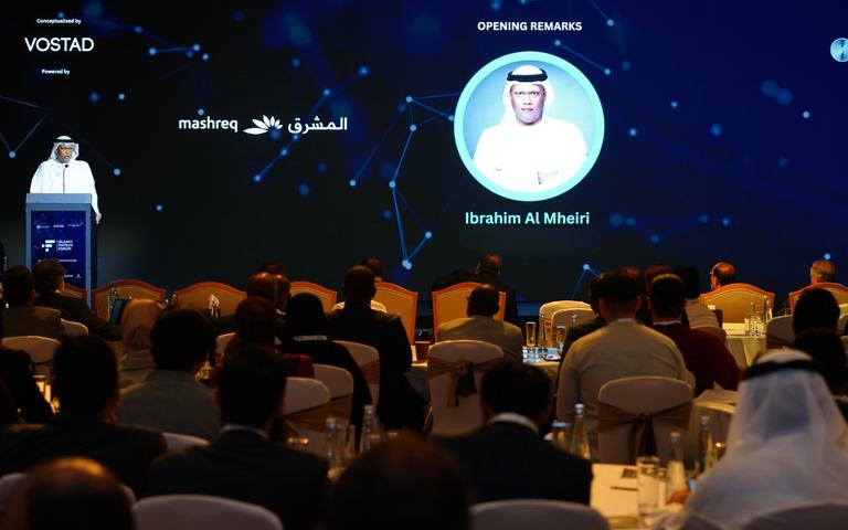 A speaker delivering opening remarks at a lectern before a seated conference audience